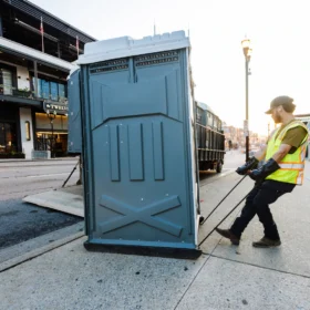 fusionsite worker delivering portable toilet on street in a downtown district